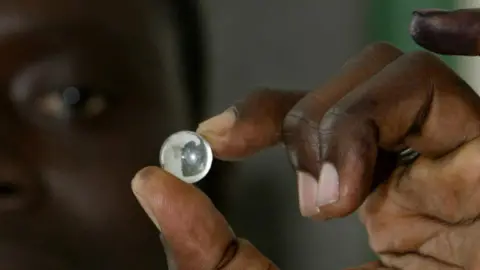 AFP A voter in Gambia holding up a marble used to vote - archive shot