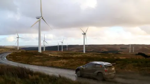 Getty Images A car drives in front of wind turbines in Newtown, Powys