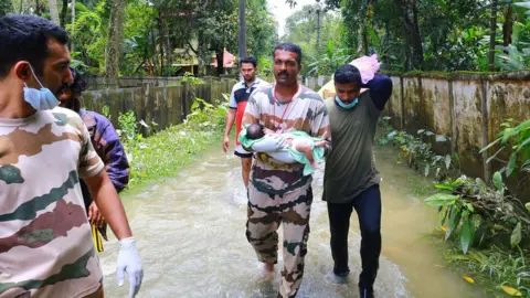 AFP A worker carries a baby boy rescued with his family in Chengannur following widespread flooding in the south Indian state of Kerala on August 20, 2018