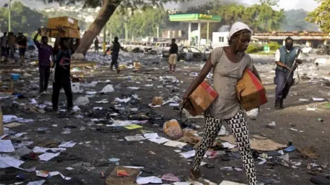 PA People carry merchandise from the Delimart supermarket complex which was burned during two days of protests against a planned hike in fuel prices in Port-au-Prince, Haiti, Sunday, July 8, 2018.