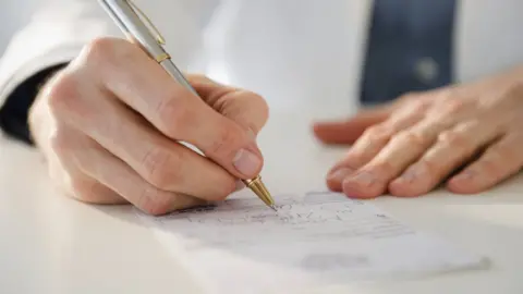 Getty/Jamie Grill Photography A doctor signing a letter