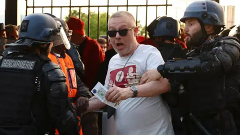 Reuters A fan is held by a police officer and a steward inside the stadium by the turnstiles as the match is delayed