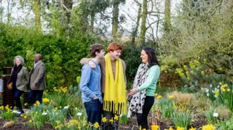 Destination Lincolnshire Three people standing among daffodils, chatting and laughing, with a couple in the background walking past the daffodils.