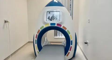 The device is a round shape with a multi colour circle and a large TV screen.