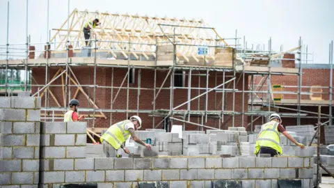 Builders wearing high-vis and hard hats laying bricks at a housing development.