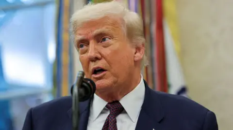 Reuters President Donald Trump, wearing a navy blue suit and red spotted tie, speaks into a microphone in the Oval Office on 6 August.
