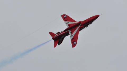 Red Arrow plane emitting blue smoke flying over Guernsey