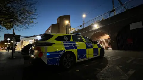 A police car parked outside Chelmsford Railway Station. The sun is setting into the photo.