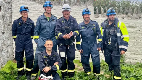 KATE FOX Six coastguards all stand together and smile, one holds the baby raven.