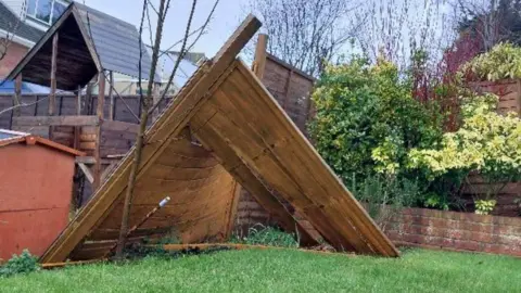 BBC Weather Watcher Yen Milne Garden with grass and walled flower bed with wooden fence strewn across.