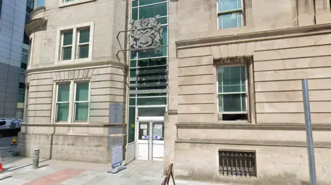 Google A general view of Cardiff Civil Justice Centre from outside. It has a small entrance with a crest above two double doors, flanked on the side with green-tinged windows
