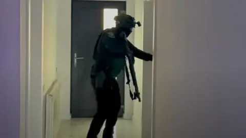 A screengrab from a video shows an armed police officer searching a house