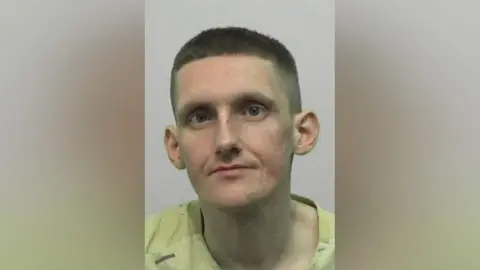 Mugshot of Daniel Allison. He is clean shaven and has short dark hair with shaved side. He is wearing a mustard yellow t shirt. 