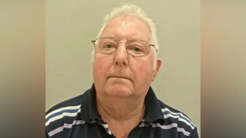 Lancashire Police A mugshot of a man in a striped polo shirt. He is wearing glasses and has grey hair. 