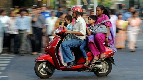 A family of four - father, mother and two children, travel on a scooter in India