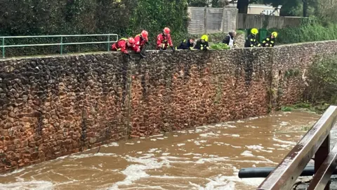 Officers from agencies look over a wall. They are looking into the river.