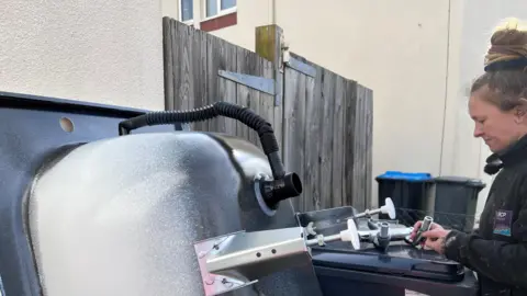 Woman screws leg into bottom of bath leaning against the wall of a house.