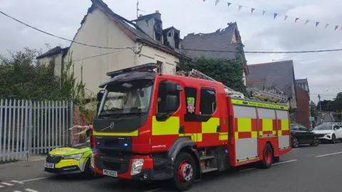 A red and yellow fire engine is parked outside a badly damaged building