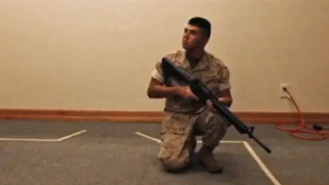 A man wearing camouflage clothing is kneeling on the floor holding a large gun.