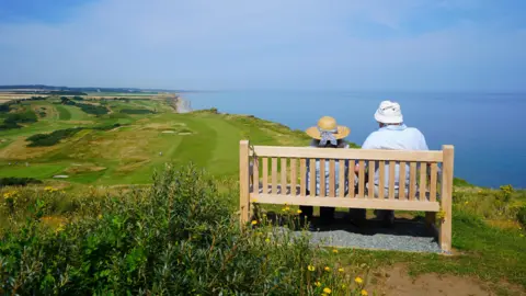 Two people sat on a bench on a cliff top at Sheringham looking out to sea