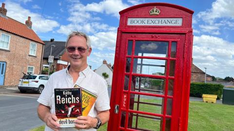 Ian Sibley-Calder stood outside the phone box holding two books