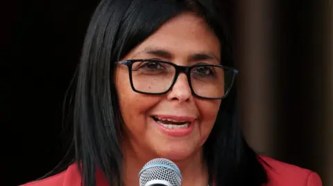 Venezuela's interim leader Delcy Rodríguez speaks into a microphone during a meeting with US Interior Secretary Doug Burgum, on 4 March. She is wearing a red jacket and black-rimmed glasses. 