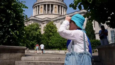 A woman wearing a long sleeved white blouse and turquoise hat shields her face from the sun