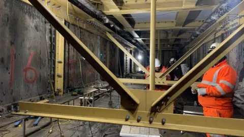 Network Rail Steel structures inside a viaduct - with construction staff wearing orange high-vis uniforms and hardhats.