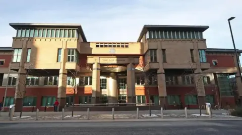 PA Media Sheffield Crown Court from the outside, a large four-storey building with pillars at the front. Four trees lines the street in front of the building and there is a line of bollards in front of a road that runs outside the court.