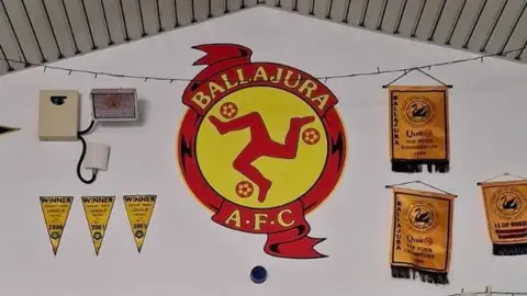 A shot of a large emblem, representing Ballajora AFC. It is visually very similar to the Manx national crest