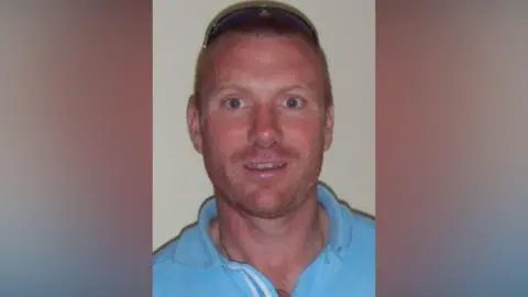 Christopher Chittock wearing a blue top with sunglasses on top of his head, he has very short hair. 