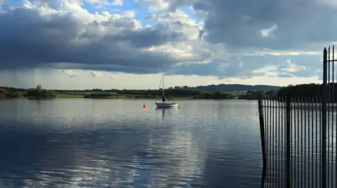 A still loch with a sailing boat in the middle of it