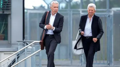 NTB/Reuters A man and a woman walk in grey suits with a fence behind them,