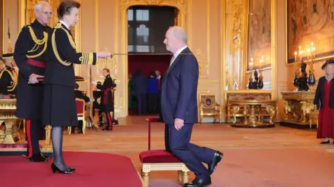 PA Media Alan Bates was given the honour by the Princess Royal who is holding the sword