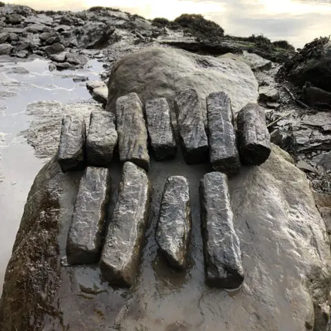 Durham University and Gary Bankhead Some of the whetstones found at the dig site. They are long, dark and rectangular. They are differing lengths and have been laid out on a large rock by the edge of the River Wear.