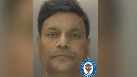 A man with dark eyes and dark face looks towards the police camera