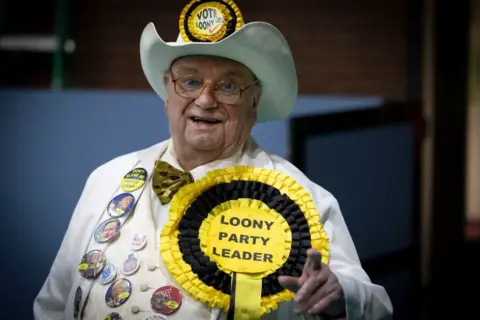Getty Images Howling Laud Hope, leader of the Monster Raving Loony party, clad in a white suit and cowboy hat decorated with buttons and a large rosette