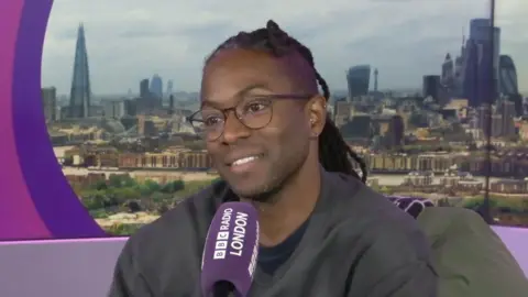 TV presenter Nigel Clarke sits in front of a purple Radio London branded microphone in a studio.