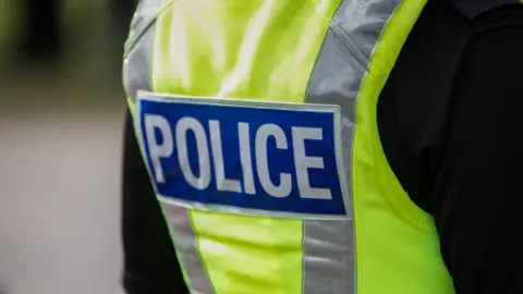 A police officer stands with his back to the camera with his fluorescent jacket showing the "police" label. 