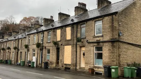 Nicola Rees/ BBC A mid-terraced house has boarded-up windows and signs of smoke damage.