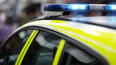 Zoomed in image of the left windows and yellow panels of a police car, with blue lights on top