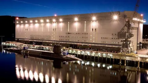 Ministry of Defence The Faslane naval base lit up at night. There is a Trident submarine in the Clyde next to the base