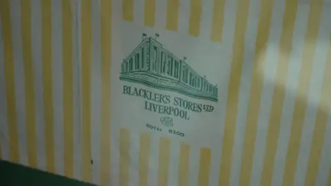 A yellow and white striped bag bearing the words Blacker's Stores Ltd written in green. 