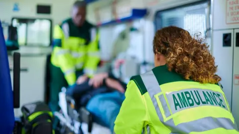 Two members of ambulance staff work together to bring a patient into an ambulance.