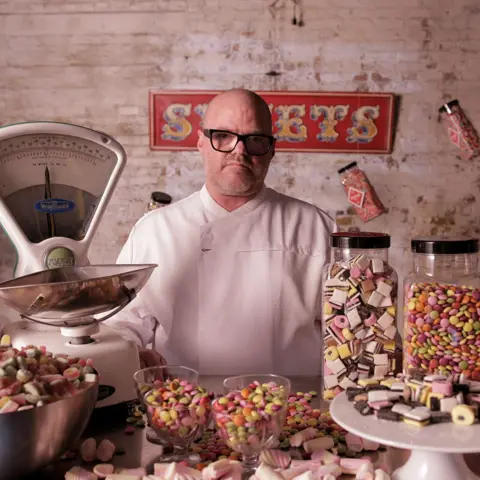 Heston Blumenthal wearing a white chef's outfit, surrounded by sweets