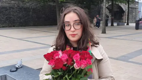 Ciara O'Connor-Pozza stands in Guildhall Square holding a bunch of red roses