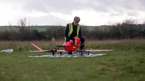 A man wearing a hi vis vest assembles a drone at an airfield in Oxfordshire