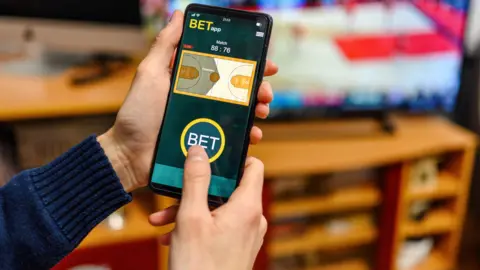 Getty Images A hand holding a mobile phone with a betting app installed.