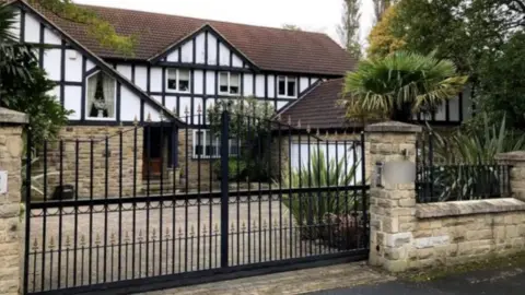A mock-Tudor fronted house sits behind iron gates.