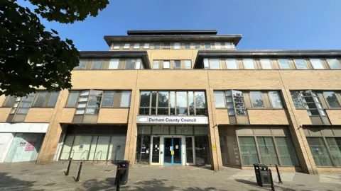A large four-storey office building with a sign reading Durham County Council above the front door. The coroner's office is on the top floor.